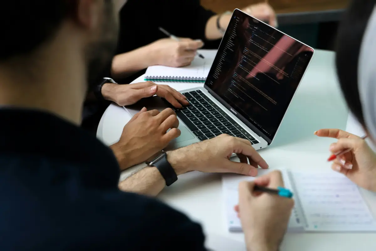 Manos sobre el teclado de una laptop y un cuaderno durante una sesión de trabajo en una mesa blanca.